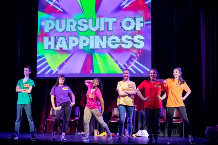 Six teenagers on stage with a large sign that reads "Pursuit of Happiness" behind them