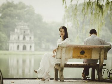 A couple sits on a bench ignoring each other