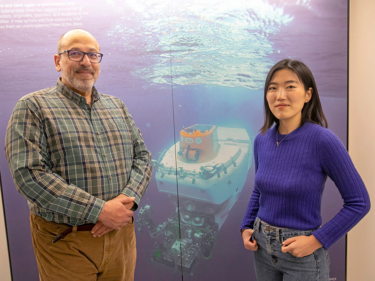 Two researchers stand in front of a large photo of a submersible they use to conduct research